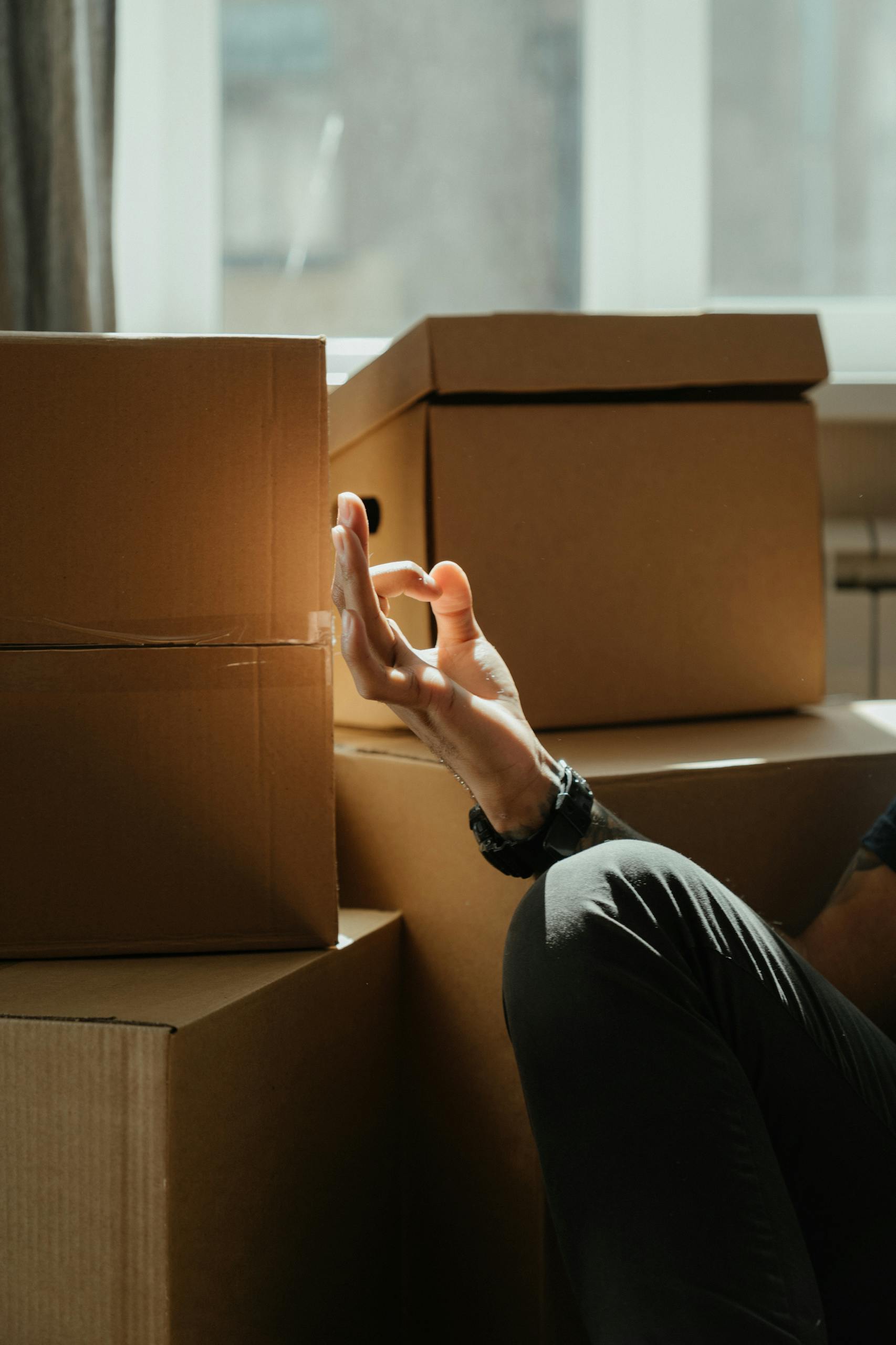 A serene moment of meditation surrounded by cardboard boxes in a sunlit room, suggesting calm during a move.